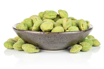 Lot of whole spicy green wasabi peanut in dark ceramic bowl isolated on white background