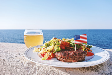 Plate with grilled juiciest burger meat and vegetables decorated with USA flag