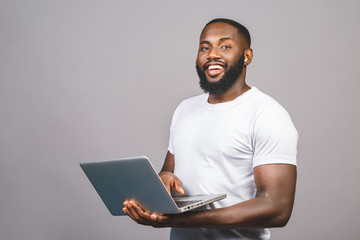 Young smiling african american man standing and using laptop computer isolated over grey background.