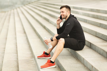 Wall Mural - Male athlete sitting on stairs, resting and talking on phone