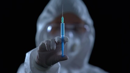 Wall Mural - Pharmacologist showing syringe at camera against black background, illegal lab