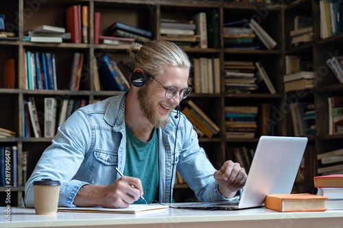 Fotografía Smiling happy young man wear wireless headset look at laptop screen make notes s