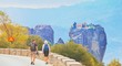 © raisondtre - Hiking young couple tramping on asphalt road in sunset from back. Travel vacation, hiking backpacking, tourism sport and people together concept. Kalambaka, Greece, Monastery Meteora fall view, Europe