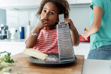 Girl Cooking With Mother In Kitchen Tasting Grated Cheese