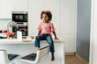 © Westend61 - Girl with laptop sitting on kitchen counter