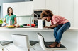 © Westend61 - Girl sitting on kitchen counter using laptop with mother in background