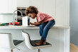 © Westend61 - Girl sitting on kitchen counter using laptop