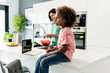 © Westend61 - Girl sitting on kitchen counter with laptop and mother in background