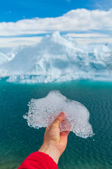 Wall Mural - Save the climate! Global warming, climate change and Environmental protection concept with icebergs on Greenland. Hand holding melting ice in front of giant iceberg in Ilulissat icefjord on Greenland.