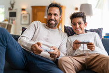 Happy Father And Son Playing Video Game On Couch In Living Room