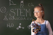 © AlesiaKan - Schoolgirl stands near the blackboard on which is written 'STEM education'. She is holding a metal robot in her hands. The concept of modern learning. STEAM. DIY. AI.