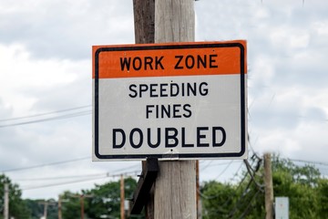 a road sign attached to a electric pole warning drivers about working zone and fine for speeding