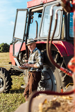Selective Focus Of Farmer In Straw Hat Using Laptop Near Tractor