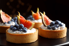 Tarts With Blueberries And Figs On Black Table Against Dark Background, Closeup. Delicious Pastries
