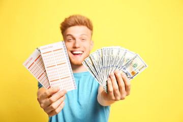 Wall Mural - Happy young man holding lottery tickets and money on yellow background