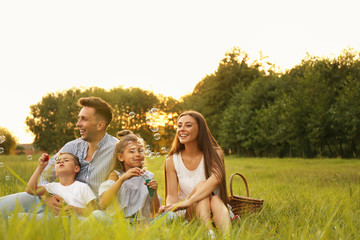 Sticker - Happy family blowing soap bubbles in park at sunset. Summer picnic