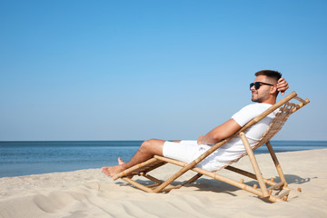 Wall Mural - Young man relaxing in deck chair on sandy beach