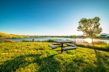 Wall Mural - Picnic table at a park with scenic view of a lake that reflects the sky and sun