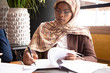 © Mangostar - Muslim African American businesswoman scanning contract. Business women wearing hijabs, sitting in cafe and reading document with pen. Signing agreement concept