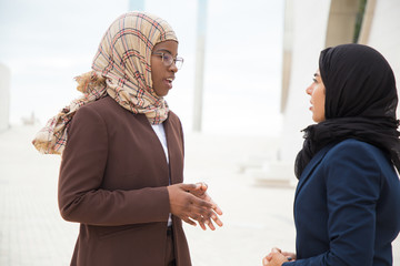 Wall Mural - Successful Muslim business colleagues chatting outside. Business women in hijabs standing outdoors and chatting. Business colleagues concept