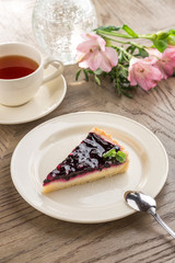 Wall Mural - piece of blueberry cheesecake with cup of black tea and flowers on wooden table