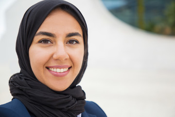 Happy confident Muslim business lady posing outside. Closeup portrait of beautiful young business woman in black hijab smiling at camera. Muslim businesswoman concept