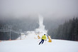 Back view of unrecognizable male downhill skiing on snow-covered snowy slope. Skier doing freeriding descenting in snowfall on deserted mountain. Ski run with chairlift. Blurred mountain views