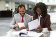 © Mangostar - Cheerful business colleagues checking documents during coffee break. Business man and woman sitting in cafe, reading documents and using tablet. Paperwork concept