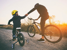 Father And Son Together Are Riding Bicycles Through The Pathway In The Field