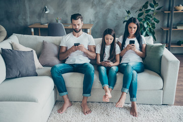 Sticker - Portrait of nice attractive lovely concentrated focused family wearing casual white t-shirts jeans denim sitting on sofa using 5g browsing at industrial style interior living-room