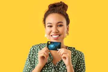 Wall Mural - Happy African-American woman with credit card on color background