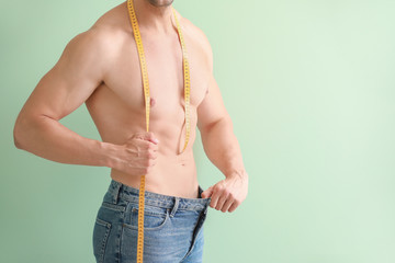 Sticker - Handsome muscular man in loose jeans and with measuring tape on color background. Weight loss concept