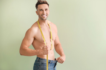 Sticker - Handsome muscular man in loose jeans and with measuring tape on color background. Weight loss concept