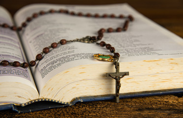 Wall Mural - Closeup open holy bible and beautiful Christian rosary beads on top main focus at Jesus Christ crucifix on wooden background.