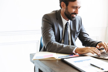 Canvas Print - Handsome young positive business man sitting in office using laptop computer working indoors.