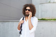 © timtimphoto - Pretty young curly male with beard walking down the street on sunny day while talking on phone, wearing white shirt and black backpack