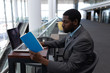 © WavebreakMediaMicro - Side view of African-American businessman with laptop sitting at table and reading a book in modern