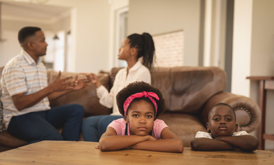 Wall Mural - African American children leaning on table while parents arguing on the sofa