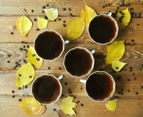 Two cups of coffee on top with autumn leaves and coffee beans on wooden background