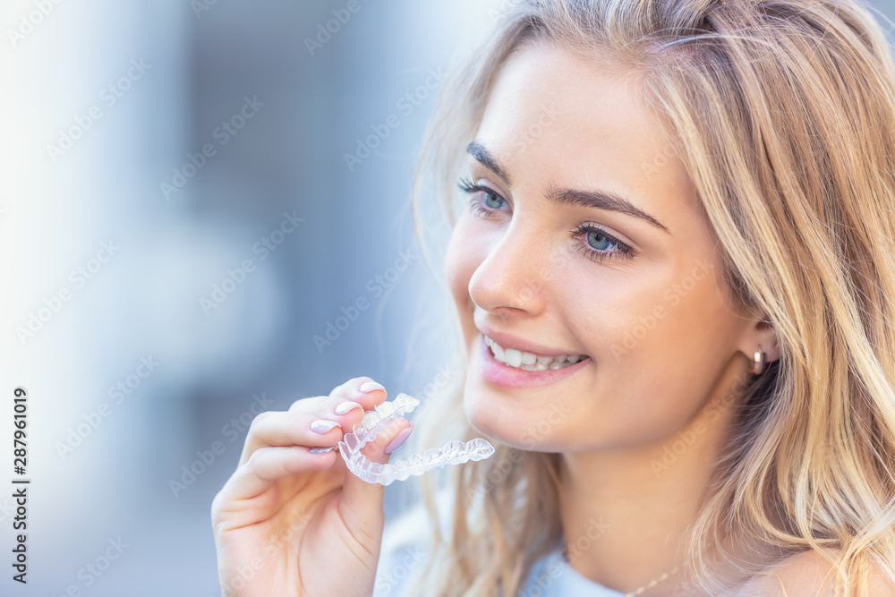 Invisalign orthodontics concept - Young attractive woman holding - using invisible braces or trainer - obrazy, fototapety, plakaty 