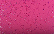 Pink confetti glitter sequins on pink background, top view