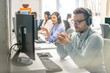 © Bojan - Friendly handsome young male call centre operator listening to a client while working in group with other customer support agents.