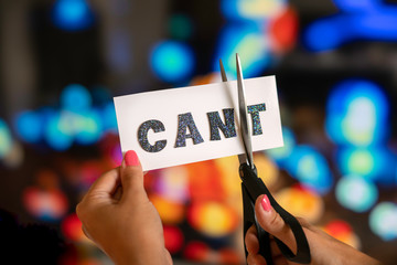 Sticker - Woman hand are cutting over white paper with scissors over the word cant and converting it to the word can. City lights bokeh as background. Motivational and inspiraton concept.