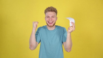 Wall Mural - Happy young man with lottery ticket under money rain on yellow background