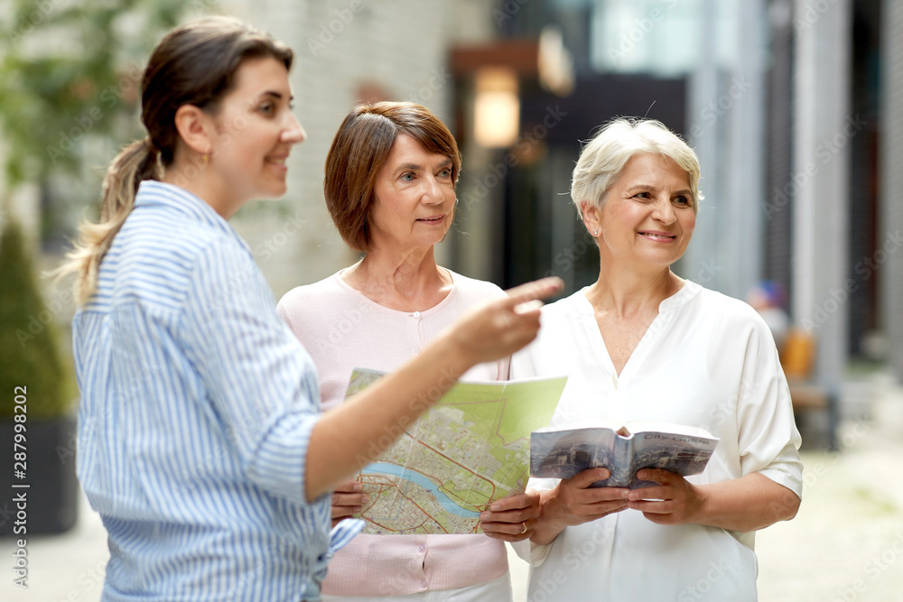 tourism, travel and friendship concept - female passerby showing direction to senior women with city guide and map on tallinn street - obrazy, fototapety, plakaty 