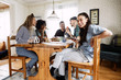 © Maskot - Portrait of smiling young woman using smart phone while sitting with friends at home