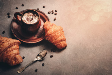 Canvas Print - Hot coffee with foam and fresh croissants on a dark rustic background in sunlight, cozy atmosphere, vintage style.