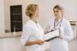 © dikushin - Two good-looking young woman doctor looking at clipboard and working on patient record while standing in the corridor next