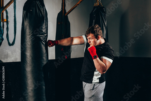 Muscular kickbox fighter exercising with punch bag at the gym Фотошпалери