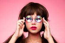 Fashion Model Looks At Camera For Shooting New Collection Sunglasses.  Beautiful Asian Woman Set Afro Hair Trend Make Up Wear Kaleidoscope Glasses With Colorful, Studio Lighting Pink Background